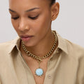 Woman wearing a gold chain necklace with a blue pendant on a plain background