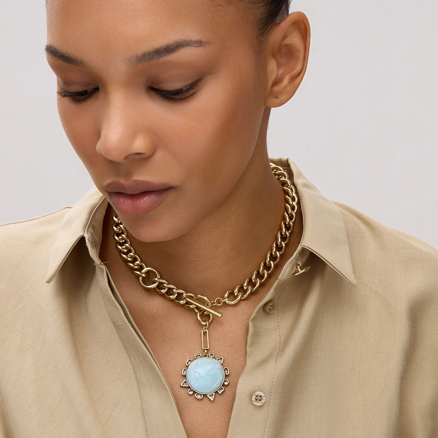Woman wearing a gold chain necklace with a blue pendant on a plain background