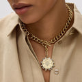 Gold chain necklace with a circular pendant worn by a person in a beige shirt.