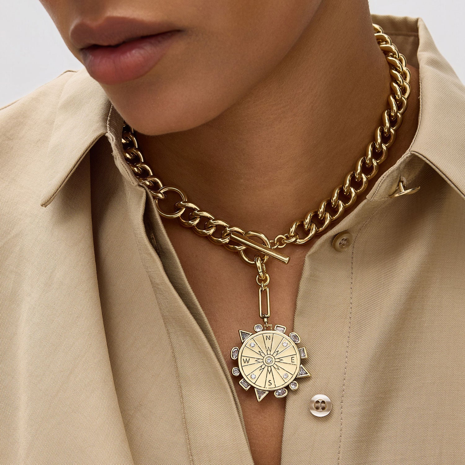 Gold chain necklace with a circular pendant worn by a person in a beige shirt.