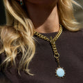 Close-up of a gold chain necklace with a blue pendant worn by a person with blonde hair.