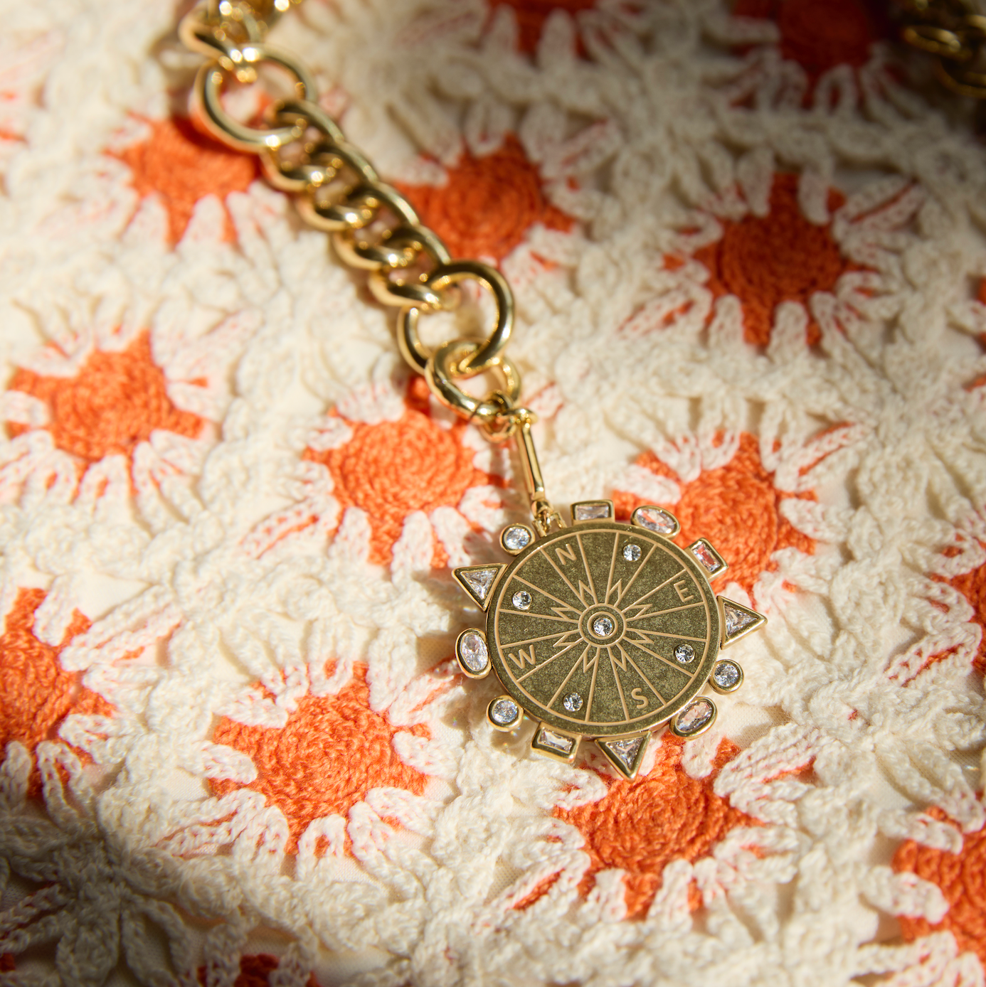 Gold compass pendant necklace on a textured fabric background